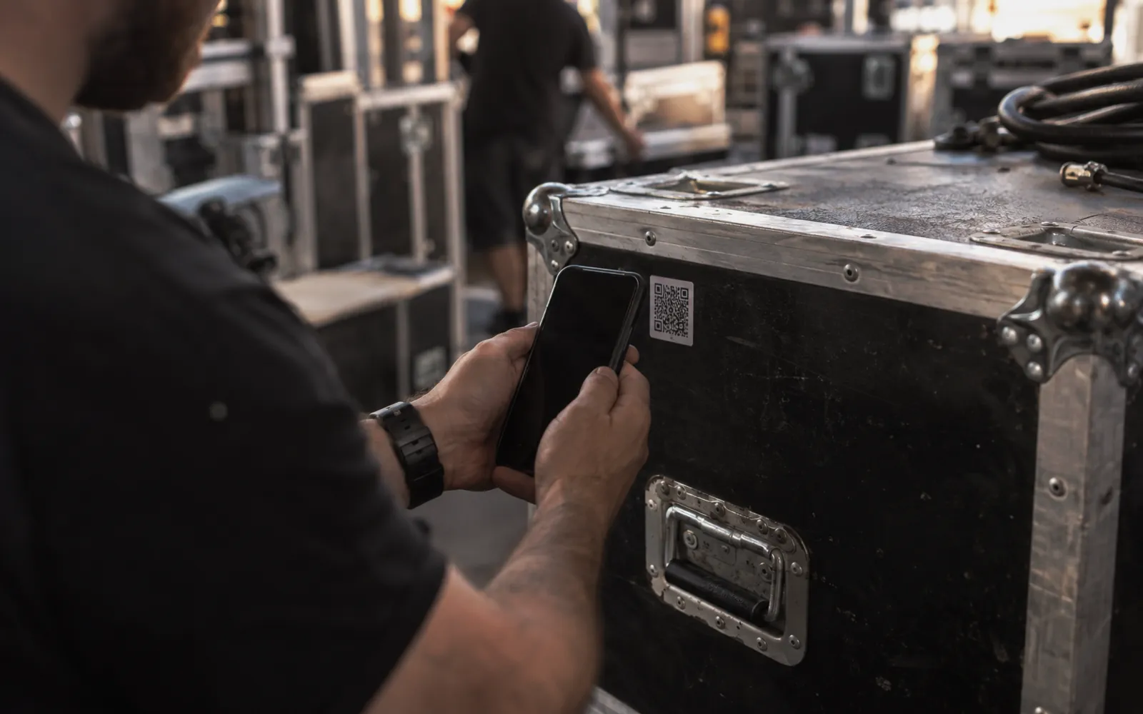 Technician's hands scanning a small code sticker on a black road case with a phone