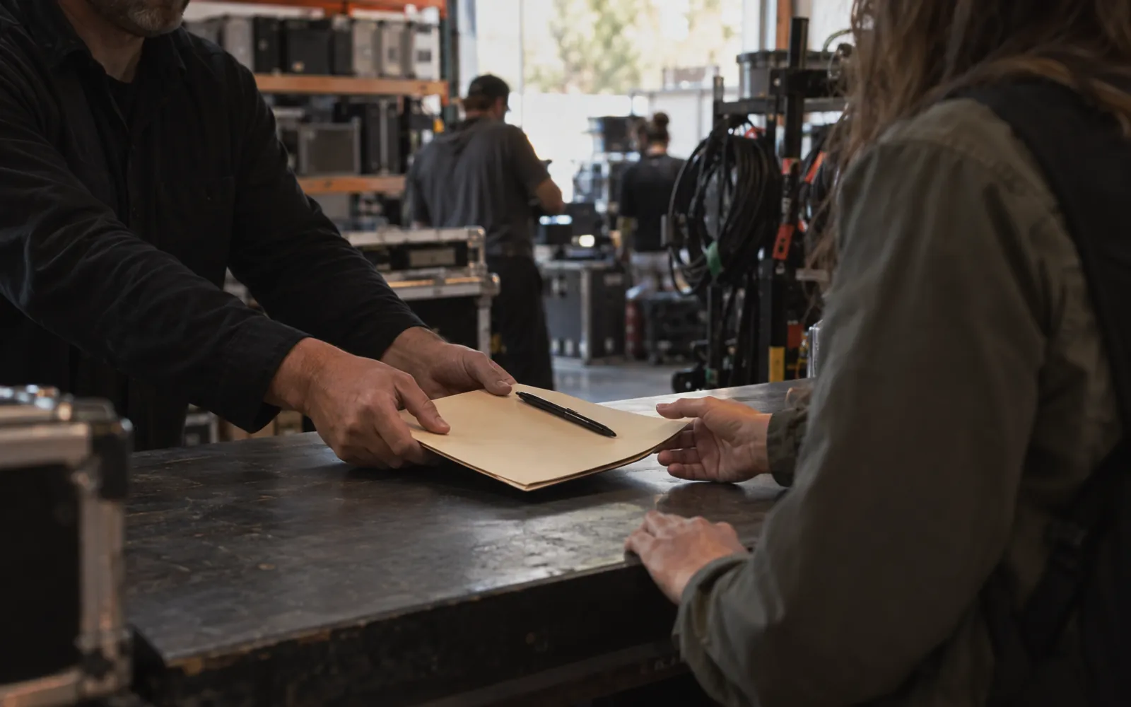 Rental-house manager sliding a contract folder across the counter to a client