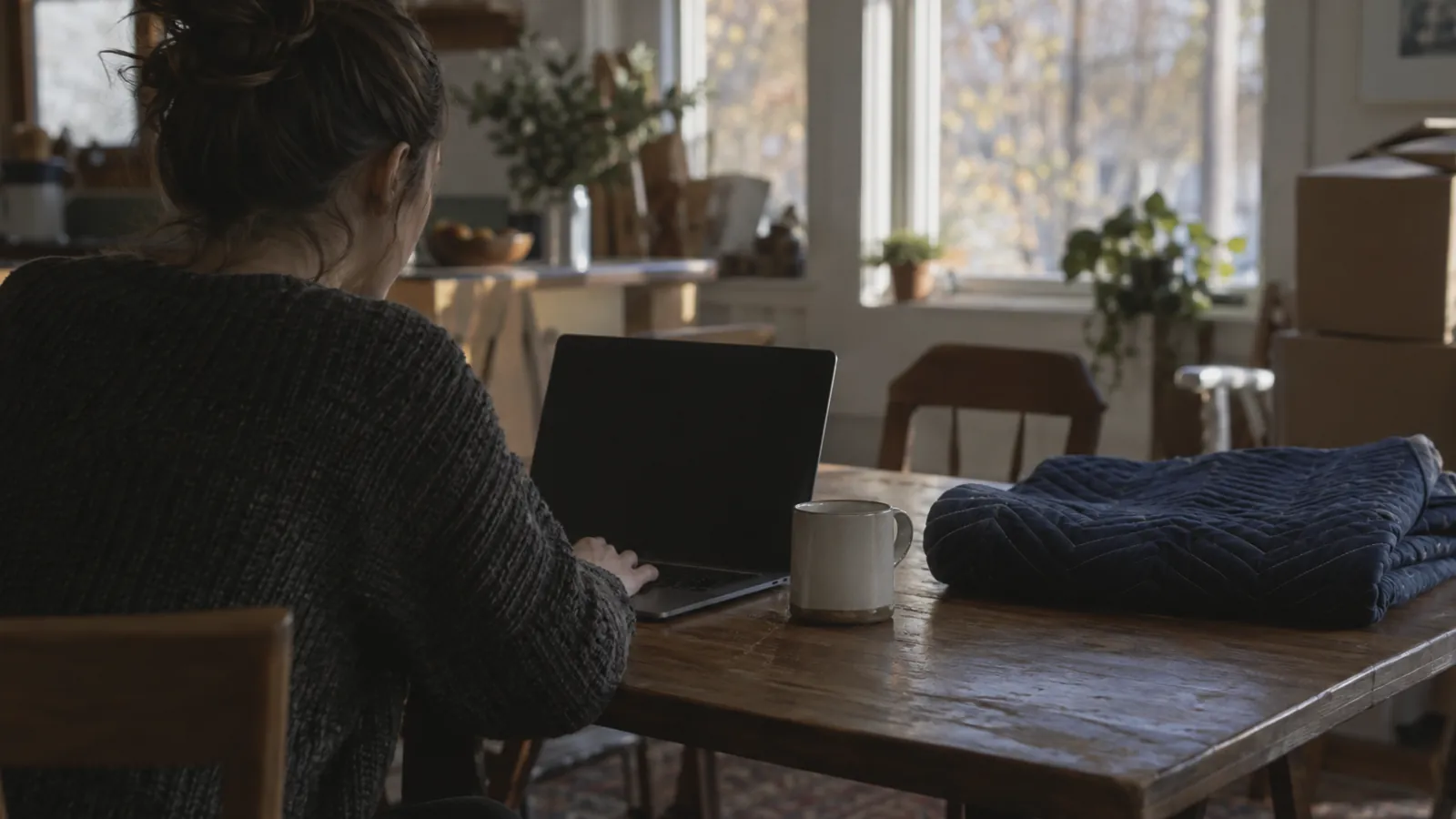 Customer at a kitchen table with a laptop, screen out of focus, morning light
